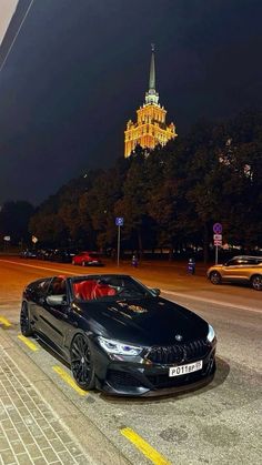 a black car is parked on the side of the road at night with a chandelier in the background