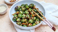 a white bowl filled with brussel sprouts and chopsticks next to bowls of seasoning