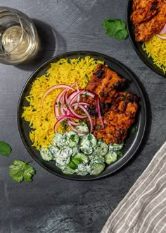 two plates filled with rice, meat and veggies next to a glass of water