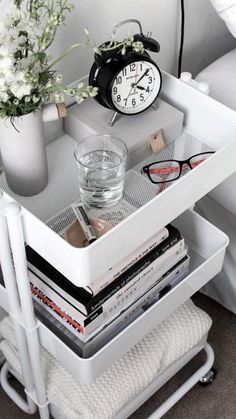 a white nightstand with books, magazines and an alarm clock on the side table next to it