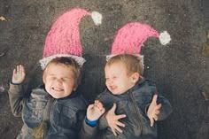 two young boys with pink hats on their heads standing in front of chalk drawings that look like they are smiling