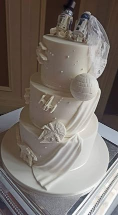 a three tiered wedding cake with white frosting and star wars decorations on top