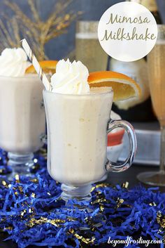 two glasses filled with whipped cream and orange slices on top of blue confetti