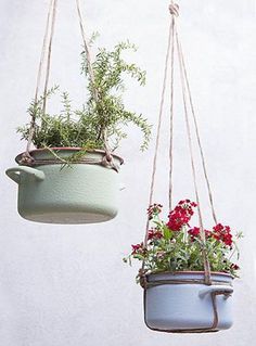 two hanging planters with plants in them on the same line, one is blue and the other has red flowers