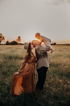 a man and woman kissing in the middle of a field at sunset with one holding his head up