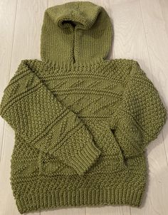 a green knitted sweater laying on top of a wooden floor