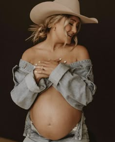 a pregnant woman wearing jeans and a cowboy hat poses for the camera with her hands on her stomach