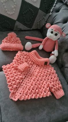 a pink crocheted outfit and hat on a couch next to a teddy bear