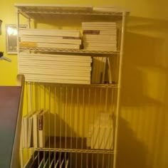 a metal shelf with books and papers on it next to a yellow painted wall in a room