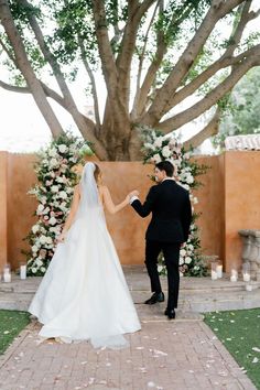 a bride and groom holding hands in front of a tree with white flowers on it