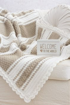 a welcome to the world sign sitting on top of a bed next to a pillow