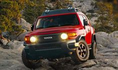 a red and black toyota truck driving on rocks