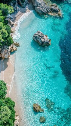 an aerial view of the blue water and sandy beach with green trees on either side