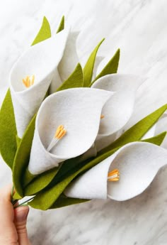 a person holding some white flowers on top of a marble countertop with green leaves