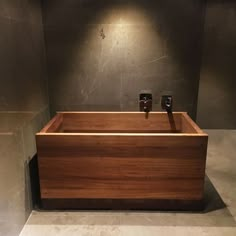 a wooden bath tub in a bathroom with grey walls and tile flooring, along with two black soap dispensers on each side