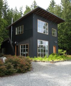 a black house in the woods with lots of windows