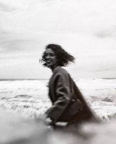 a woman is walking along the beach with her hair blowing in the wind and smiling