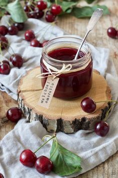 a jar filled with cherries sitting on top of a wooden table next to leaves