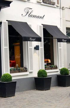 three black planters with green topiary plants in front of storefronts on cobblestone street