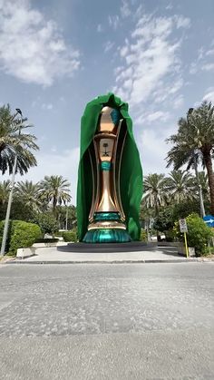 a large green and gold clock sitting in the middle of a street next to palm trees