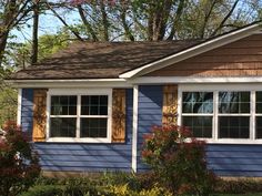 a blue house with brown shingles and white trim on the windows is surrounded by trees