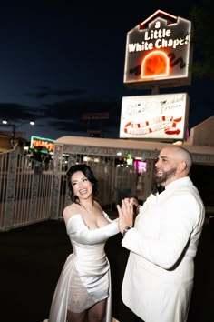 a man and woman standing next to each other in front of a white chapel sign