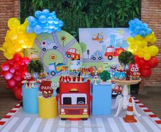 a table topped with balloons and toys next to a firetruck cake stand on top of a checkered table cloth