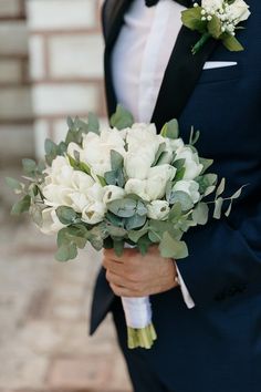 a man in a tuxedo holding a bouquet of white flowers and greenery