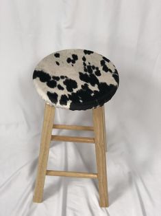 a wooden stool with black and white cow print on it's seat cover, against a white background