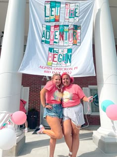 two women standing next to each other in front of a banner with letters on it