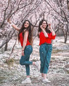 two young women are standing in front of some trees with pink flowers on them and one is holding her hands up to her face