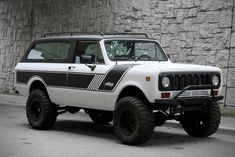 a white and black jeep parked in front of a stone wall