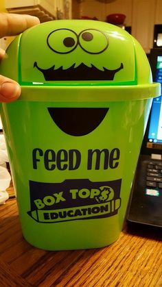 a green trash can sitting on top of a wooden table next to a laptop computer