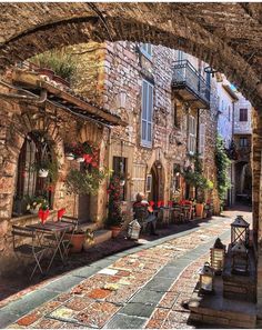 an alley way with tables and chairs on the side, surrounded by stone buildings that are lined with potted plants