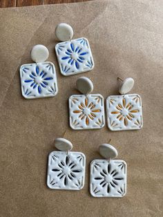 four white and blue ceramic earrings sitting on top of a piece of brown paper next to each other