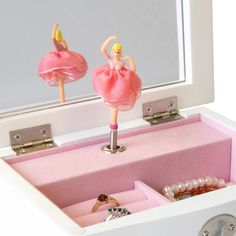 a pink ballerina doll is sitting in a jewelry box with its reflection in the mirror