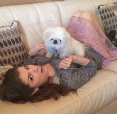 a woman laying on top of a couch holding a white dog