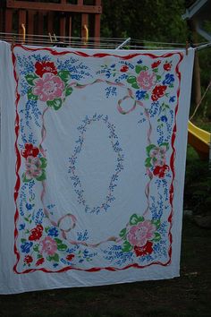 a white quilt hanging on a clothes line with red, blue and green flowers around it