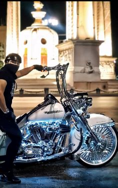 a man standing next to a parked motorcycle in front of a clock tower at night