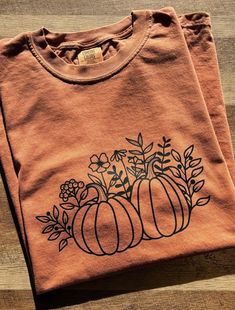 a t - shirt with pumpkins and flowers on it sitting on a wooden surface