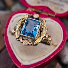 This lovely vintage ring features a lab created blue spinel in a full bezel setting that is decorated with a foliate motif halo. The ring is crafted in patinated 10k yellow gold and is currently a size 6.5. Vintage Blue Sapphire Ring With Bezel Setting, Antique 14k Gold Topaz Ring, Antique 14k Gold Topaz Ring Gift, Antique Gold Topaz Ring With Center Stone, Vintage Blue Sapphire Ring With Halo Setting, Victorian Blue Topaz Ring, Vintage Blue Ring With Bezel Setting, Vintage Blue Halo Setting Jewelry, Vintage Blue Cluster Ring With Center Stone