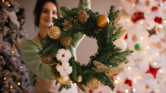 a woman holding up a christmas wreath in front of a decorated tree with gold, white and green ornaments