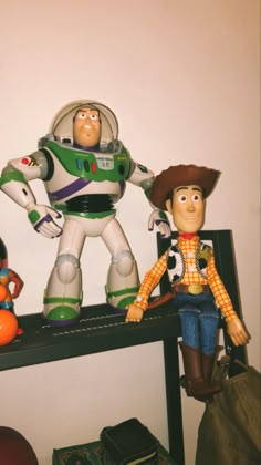 two toy figures are sitting on a shelf next to a bag and suitcase, one is buzz lightyear