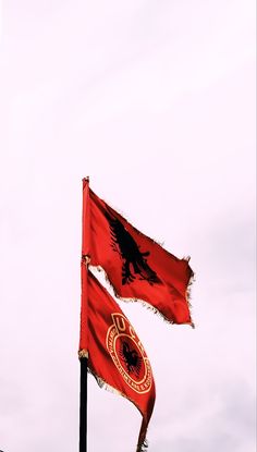 two red flags flying in the wind on top of a building under a cloudy sky