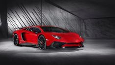 a red sports car is parked in an empty room with concrete walls and flooring