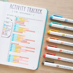 an open notebook with markers and pens on it, next to several other ones that are labeled activity tracker