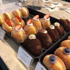 several trays of pastries with strawberries on top and other desserts in the background