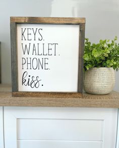 a sign that says keys wallet phone kiss on top of a shelf next to a potted plant