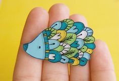 a small blue and yellow fish brooch sitting on someone's hand in front of a yellow background