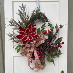 a christmas wreath on the front door with poinsettis and pineconis